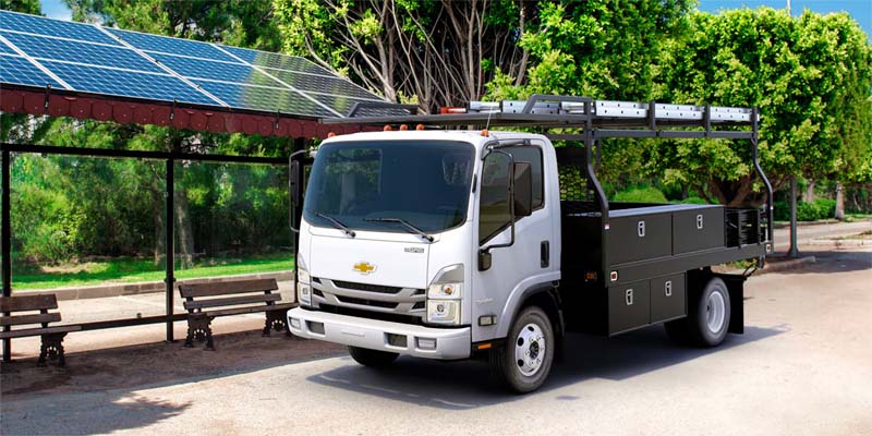 A white 2024 Chevrolet Low-Cab-Forward parked on a paved area with trees and benches behind it.
