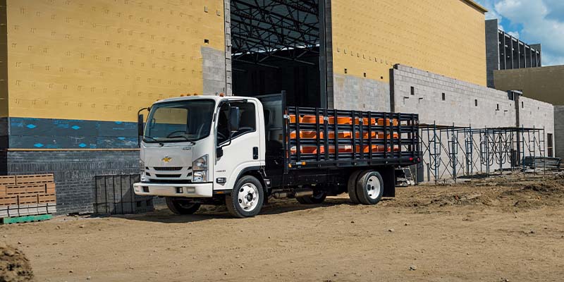 A white 2024 Chevrolet Low-Cab-Forward in a cargo configuration parked beside a building with stacked crates.