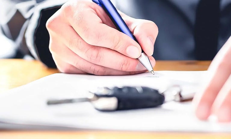 A person signing a document with a keyfob on top of the papers
